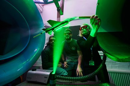 Lecturer demonstrating wind tunnel to two students wearing goggles with laser green light