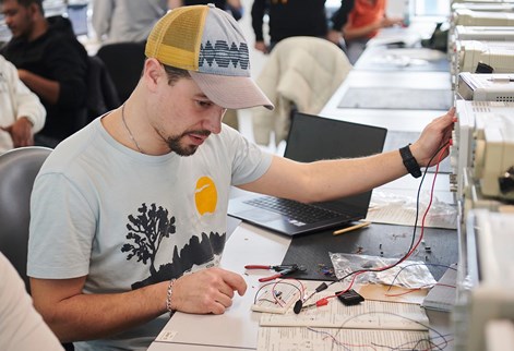 Student in electrical engineering lab working with a laptop, worksheet and circuit testing equipment