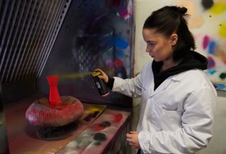 Female product design student spraying object in spray booth