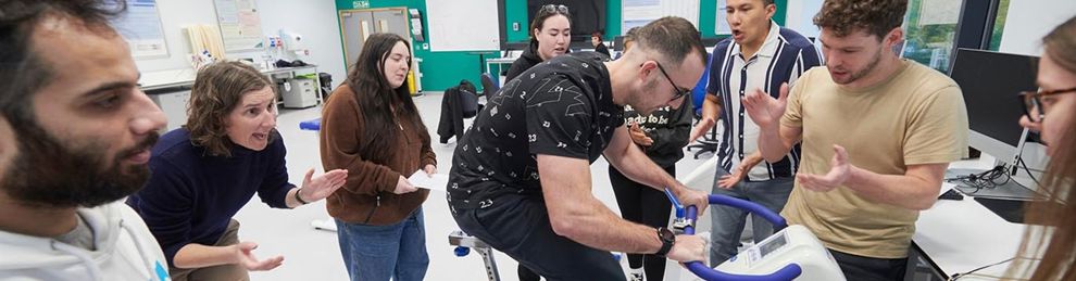 students encouraging another to pedal harder on a bike