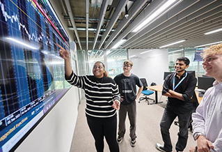 A student giving a presentation in front of a screen showing various graphs