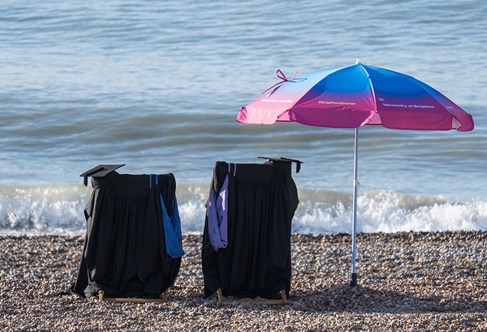 Brighton university graduation attire on deck chairs on Brighton beach 