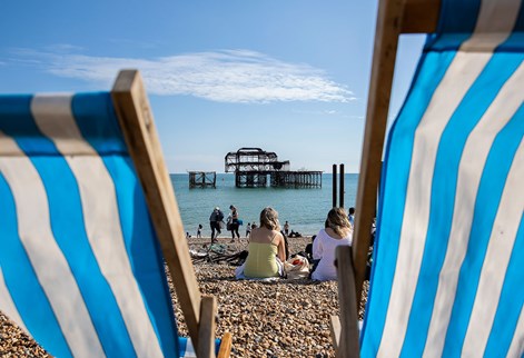 Close up of busy Brighton beach with blue and white deck chairs framing the west pier remains