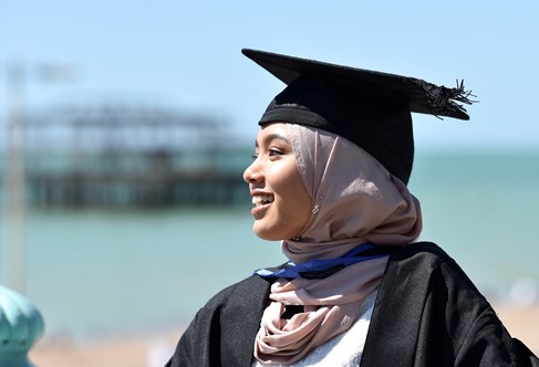 Student on graduation wearing a gown and cap infront of the sea