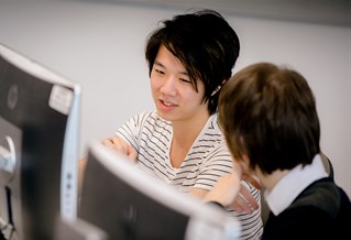 Two people talking whilst sitting at computers